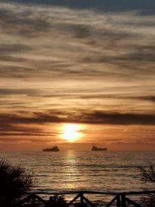una puesta de sol sobre el océano con barcos en el agua en Essenza del Mare Home en Livorno