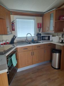 eine Küche mit Holzschränken, einem Waschbecken und einem Fenster in der Unterkunft Millfield caravan site, caravan L6 in Ingoldmells
