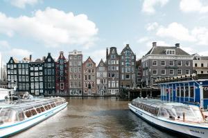 due barche sono ormeggiate in un fiume con edifici di Hotel van Gelder ad Amsterdam