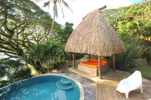 a pool with a chair and a hut next to a swimming pool at Beachfront Villa - House of Bamboo, Infinity Pool in Savusavu