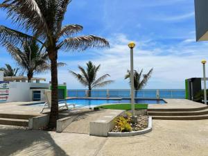 a swimming pool with palm trees and the ocean at Paradise departamento para vacacionar in Crucita