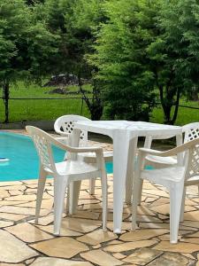 - une table et des chaises blanches à côté de la piscine dans l'établissement Sitio Serenar Chalés Equipados, à Penedo