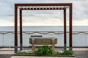 un banco de madera sentado bajo un pabellón cerca del océano en Sunset Avenue for couple w/ jacuzzi spa hot water, en Paul do Mar