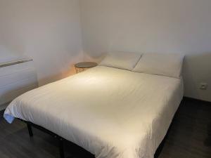 1 cama con sábanas blancas y almohadas en una habitación en Grand studio avec salon et cuisine toute équipée, en Le Creusot