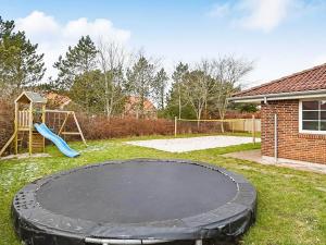 a black trampoline in a yard with a playground at Holiday home Blåvand CCCVIII in Blåvand