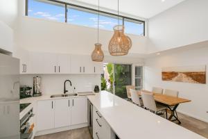 une cuisine avec des armoires blanches et une table avec des chaises dans l'établissement Sunfish Special - Beachside Townhouse by uHoliday, à Kingscliff
