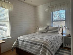 a bedroom with a bed with a striped comforter and two windows at Retreat near Beaches in Gloucester