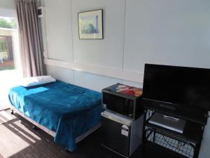 a bedroom with a bed and a flat screen tv at Rangiora Eco Holiday Park in Fernside