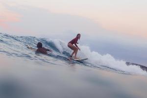 two people riding a wave on surfboards in the ocean at Hilltop Cabanas in Komari