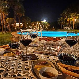 una mesa con copas de vino y comida junto a una piscina en Le stanze dei Mori - quadrupla con bagno privato en Mascalucia
