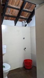 a bathroom with a toilet and a red bucket at Crossroads Hostel 1957 in Wayanad