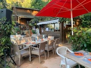 un patio con mesas, sillas y una sombrilla roja en Gîtes les Chalets Vezzani Spa, en Vezzani