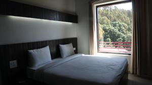 Schlafzimmer mit einem Bett und einem großen Fenster in der Unterkunft Just Naturals Wellness Resort Nainital in Bhowāli