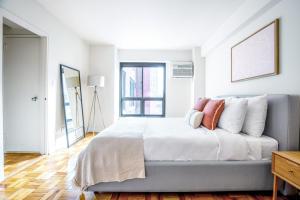 Schlafzimmer mit einem Bett mit weißer Bettwäsche und orangefarbenen Kissen in der Unterkunft Midtown E 1BR w WD Doorman nr Central Park NYC-532 in New York