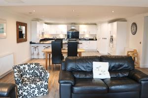a living room with a leather couch and a kitchen at BY THE BEACH, spacious apartment in Saint Merryn