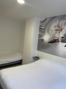 ein Schlafzimmer mit einem weißen Bett und einem Blumengemälde an der Wand in der Unterkunft Hotel Restaurant L'Escale in Sainte-Nathalène