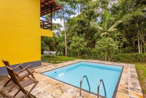 uma piscina com uma cadeira e uma casa amarela em Sítio Borges em Petrópolis