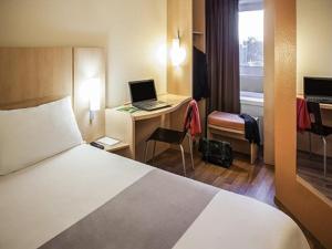 トゥールーズにあるibis Toulouse Pont Jumeauxのベッド、デスク、ノートパソコンが備わるホテルルームです。