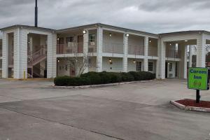 un gran edificio de apartamentos con una señal verde delante de él en Carom Inn a Travelodge by Wyndham Denham Springs-Baton Rouge en Denham Springs