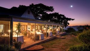 a restaurant with white tables and chairs at night at Camp Figtree by The Oyster Collection in Addo