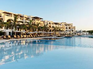 une grande piscine avec des chaises, des palmiers et des bâtiments dans l'établissement Fanar Hotel & Residences, à Salalah