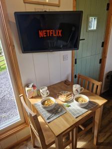 a television hanging above a wooden table with bowls of food at Elephant View Shepherds Hut in Caernarfon