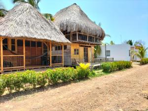 a house with a thatched roof next to a dirt road at Bungalow Palmar del Viento in Moñitos