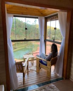 a woman sitting in a chair on a porch looking out a window at Chalés Villa Caravaggio in Santa Teresa