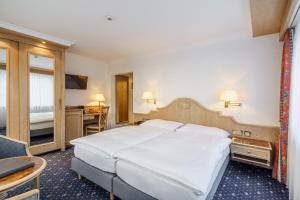 a bedroom with a large white bed and a desk at Hotel Alpenroyal in Zermatt