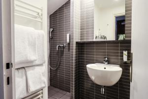 baño de azulejos negros con lavabo y ducha en Hotel Des Cedres, en Orléans