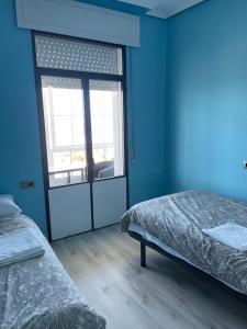 a blue room with two beds and a sliding glass door at Alojamiento Camino Portugues Oia in Villadesuso