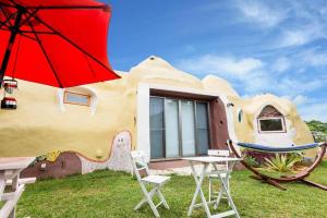 una casa con un paraguas rojo delante de ella en 土と音の旅チオンの家, en Onna