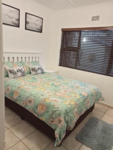 a bedroom with a bed with a floral comforter and a window at Windsor Place 6 in Uvongo Beach