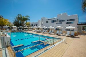 a swimming pool with chairs and umbrellas next to a building at Flouressia Gardens in Protaras
