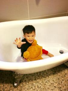 Ein kleiner Junge, der in einer Badewanne sitzt und einen Teddybären hält. in der Unterkunft 東津左岸民宿 in Yilan