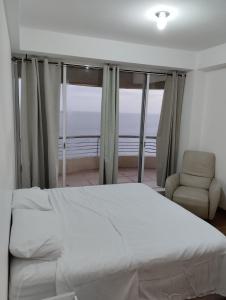 a bedroom with a bed and a chair and windows at Apartamento a la orilla de la playa en Pampatar, Isla de Margarita in Pampatar