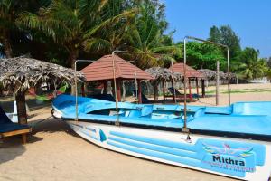 a blue boat sitting on the beach with umbrellas at Mithra Paradise Beach Hotel in Nilaveli