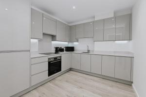 a white kitchen with white cabinets and a wooden floor at Khayat Homes - The Curve - One Bed in London