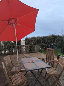 une table et deux chaises avec un parapluie rouge dans l'établissement Location résidence Océane, à Soulac-sur-Mer