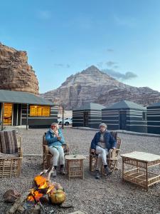 two people sitting in chairs next to a fire at Desert Jewel Camp in Wadi Rum