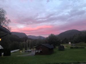 a building in a field with a sunset in the mountains at Døskelandslia Camping in Sygna