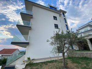 a white building with glass balconies next to a tree at A. Montenegro in Dobra Voda