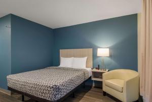 a bedroom with a bed and a chair and a lamp at WoodSpring Suites Jacksonville Orange Park in Orange Park
