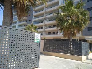 a fence in front of a building with palm trees at Piso nuevo con piscina cerca de parque las familias y playa de Almeria in Almería