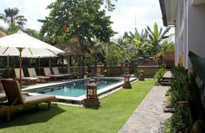 uma piscina com espreguiçadeiras e um guarda-sol em Papaya Guesthouse em Canggu