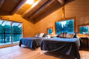 2 camas en una habitación con paredes y ventanas de madera en Les Chalets Tourisma - Chalet en bois rond avec spa et lac privé - Le Caribou en Sainte-Catherine