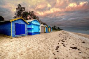 Beach Days Family Escape, Dromana في درومانا: صف من اكواخ الشاطئ الأزرق على شاطئ رملي