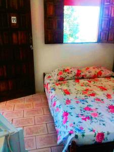 a bedroom with a bed with a floral comforter and a window at Pousada da Adélia in Itaúnas