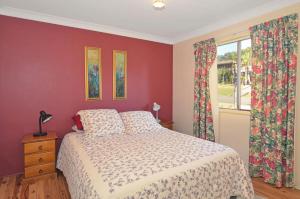 a bedroom with a bed with red walls and a window at Pipers Run - Belle Escapes Jervis Bay in Vincentia