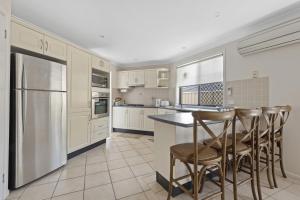 a kitchen with white cabinets and a island with bar stools at Villa Serene - Belle Escapes Jervis Bay in Vincentia